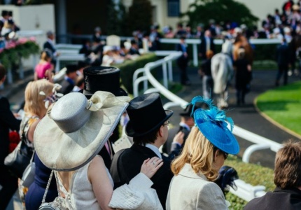 Attendees in formal wear at a horse racing event, with elegant hats and a top hat, conveying a high-profile social gathering.