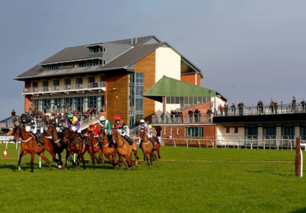 Action-packed horse racing at Carlisle Racecourse with jockeys competing and spectators watching from the grandstand